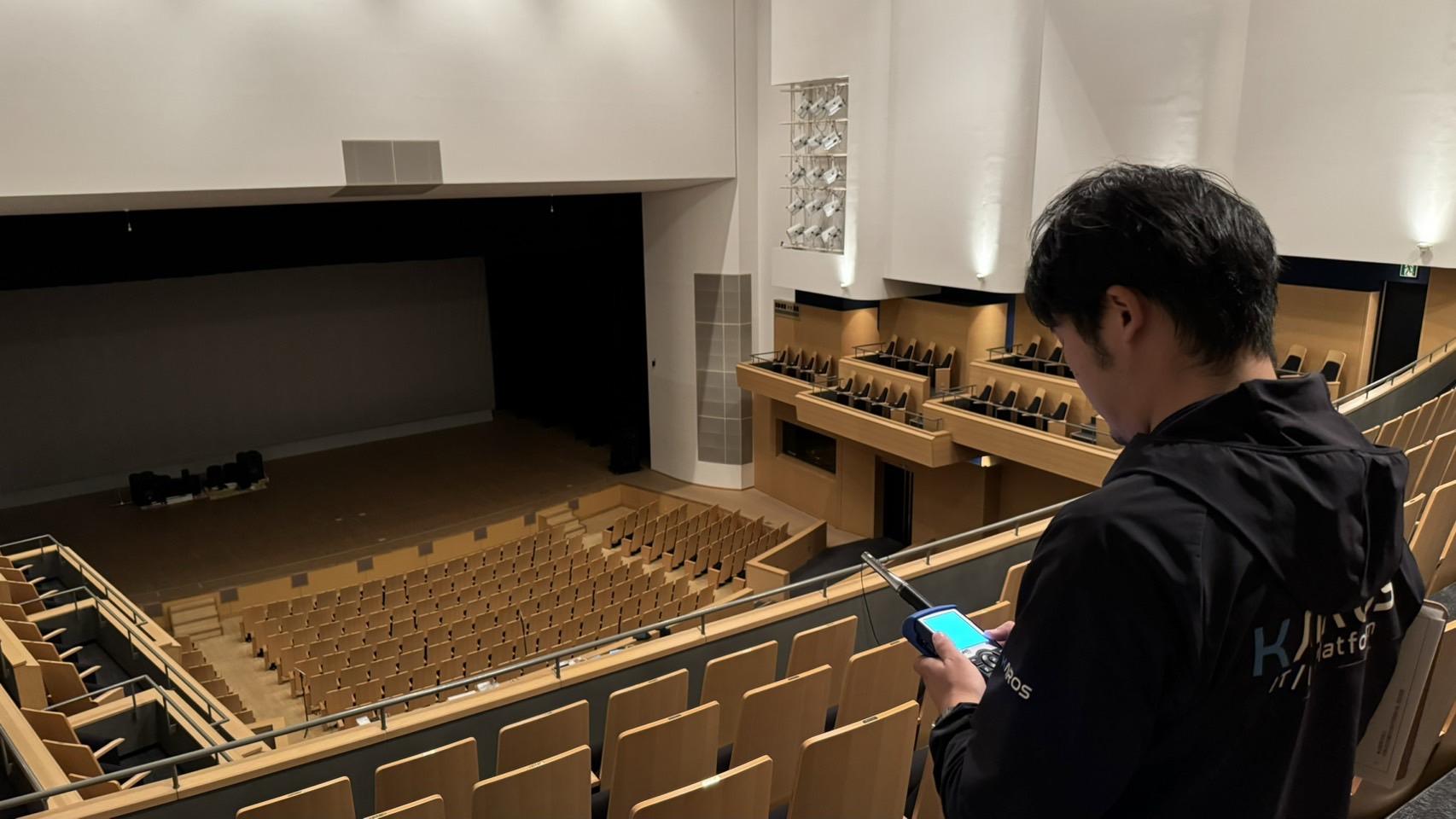 大ホールで音響測定器を使って現地調整を行う正清電器の技術者